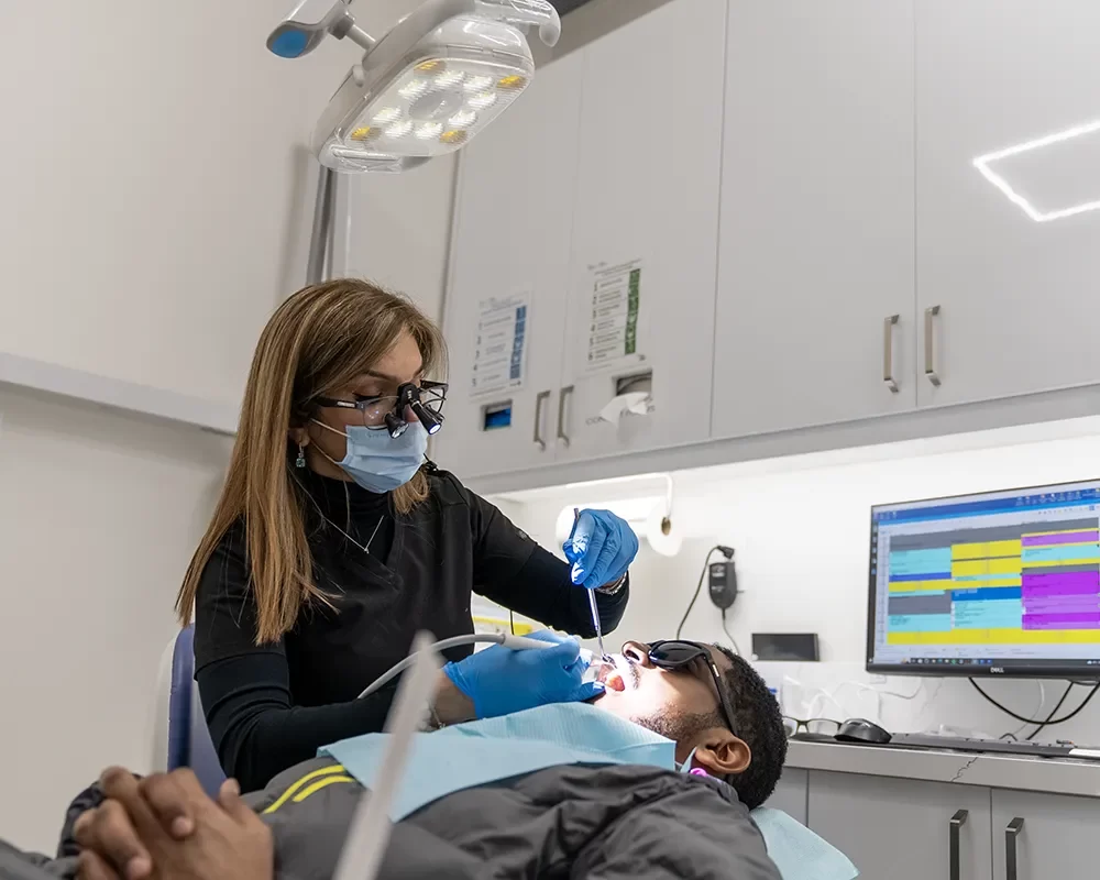 A man in a dentist chair holds a mirror during a dental cleaning session at Dental Cleaning in St. Clair
