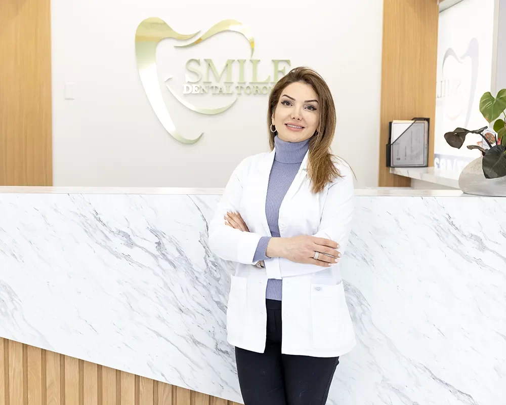 Dr. Rashin Elahi standing in front of Smile Dental Toronto logo with a bright smile, representing quality dental care
